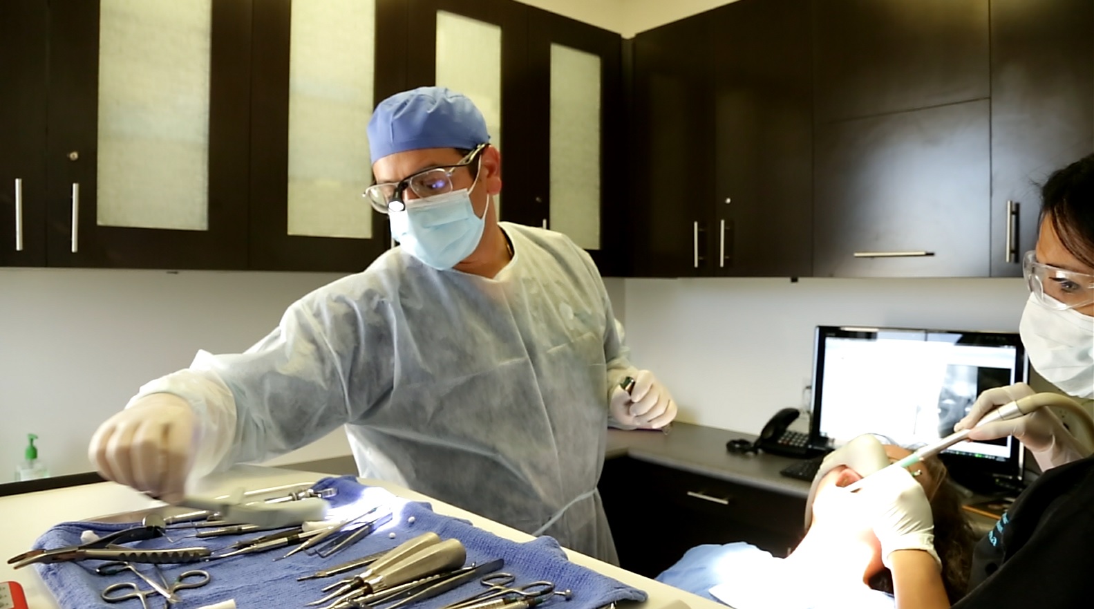 Dr. Nader Salib, DDS, performing oral surgery in the operatory with a surgical assistant