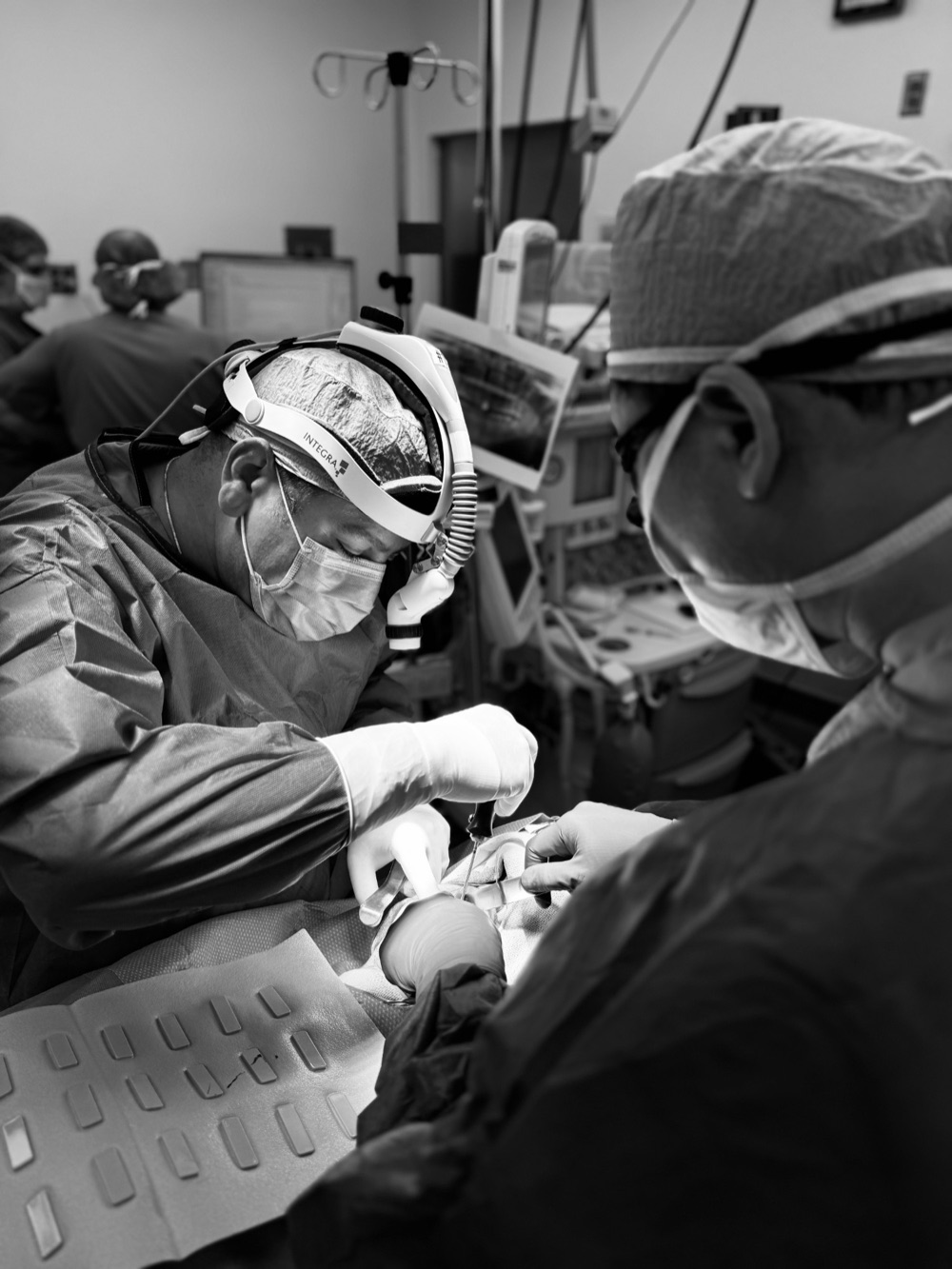 Dr. Nader Salib performing surgery in a hospital operating room, wearing surgical loupes and a headlight